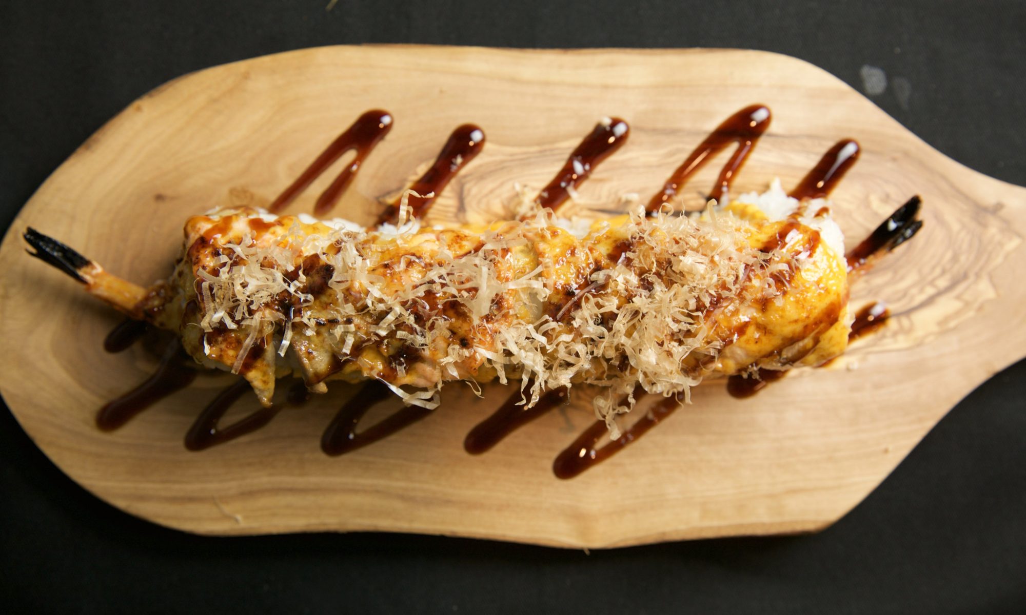 closeup overhead view sushi roll on wooden board with soy drizzle